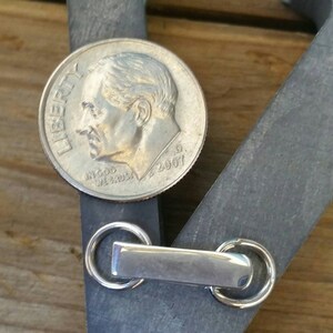 Peut inclure: Une pi&egrave;ce de monnaie argent&eacute;e de 2007 est pos&eacute;e sur un objet en m&eacute;tal gris fonc&eacute; avec une barre rectangulaire et deux anneaux circulaires. La pi&egrave;ce est &agrave; c&ocirc;t&eacute; de l'objet m&eacute;tallique, sur une surface en bois.