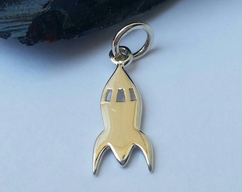 May include: A silver rocket ship charm with a loop for attaching to a necklace or bracelet. The charm is about 1 inch tall and has a shiny finish.