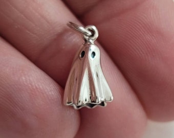 May include: A small, silver ghost charm with a loop for hanging. The ghost has a draped form with a scalloped bottom edge and two small, dark blue eyes. This charm is suitable for Halloween or spooky-themed jewelry.