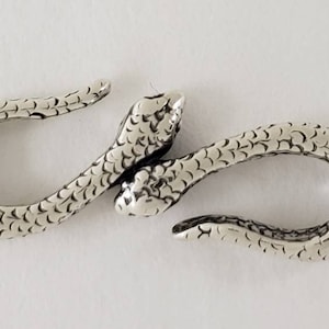 Puede incluir: Cierre de serpiente plateado con superficie texturizada. El cierre est&aacute; dise&ntilde;ado para conectar dos piezas de joyer&iacute;a o una correa.