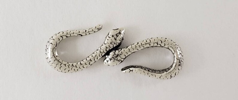 Puede incluir: Cierre de serpiente plateado con superficie texturizada. El cierre est&aacute; dise&ntilde;ado para conectar dos piezas de joyer&iacute;a o una correa.
