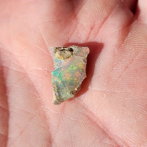 May include: A rough, irregular piece of opal with a milky white base and iridescent flashes of green, blue, and orange.