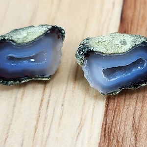 May include: Two halves of a geode with a light blue interior and a dark green exterior. The geode is sitting on a wooden surface.