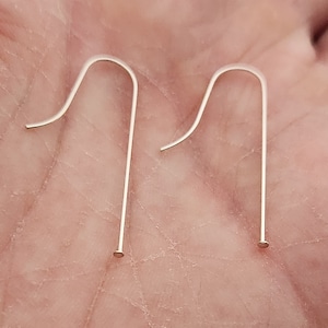 May include: Two silver-colored earring hooks. Each hook has a curved top and a straight, thin post ending in a small, flat disc. The hooks are displayed against a neutral background.