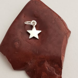 May include: A silver star charm pendant on a red background.