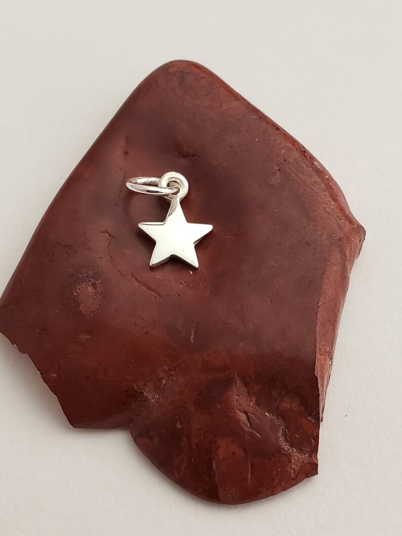 May include: A silver star charm pendant on a red background.