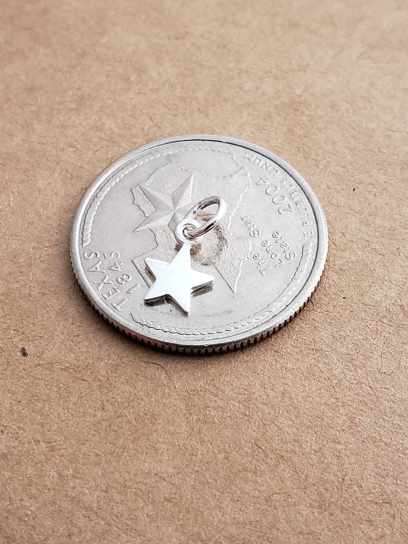 May include: A silver charm in the shape of a five-pointed star, shown next to a US quarter with the year 2004 and the state of Texas.