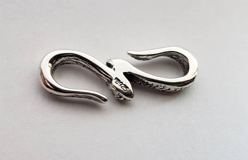 Puede incluir: Cierre de plata en forma de serpiente con una superficie texturizada y un sello 925. El cierre est&aacute; dise&ntilde;ado para ser utilizado para joyas u otros accesorios.