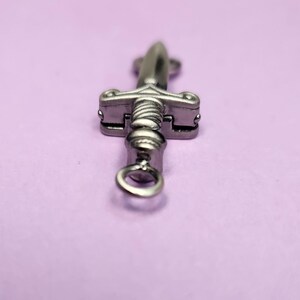 May include: A silver sword charm with a loop at the bottom for attaching to a necklace or bracelet.