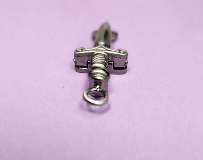 May include: A silver sword charm with a loop at the bottom for attaching to a necklace or bracelet.