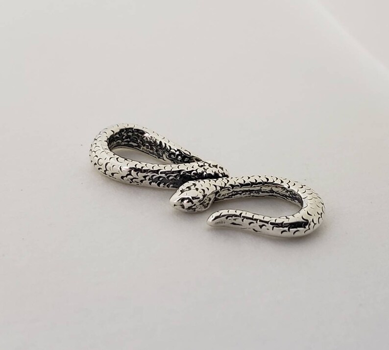 Puede incluir: Cierre de serpiente de plata con superficie texturizada. El cierre est&aacute; dise&ntilde;ado para ser utilizado como conector para joyas u otros accesorios.