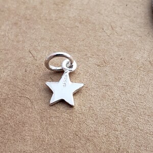 May include: A silver star charm with a jump ring. The back of the charm has the inscription "925".