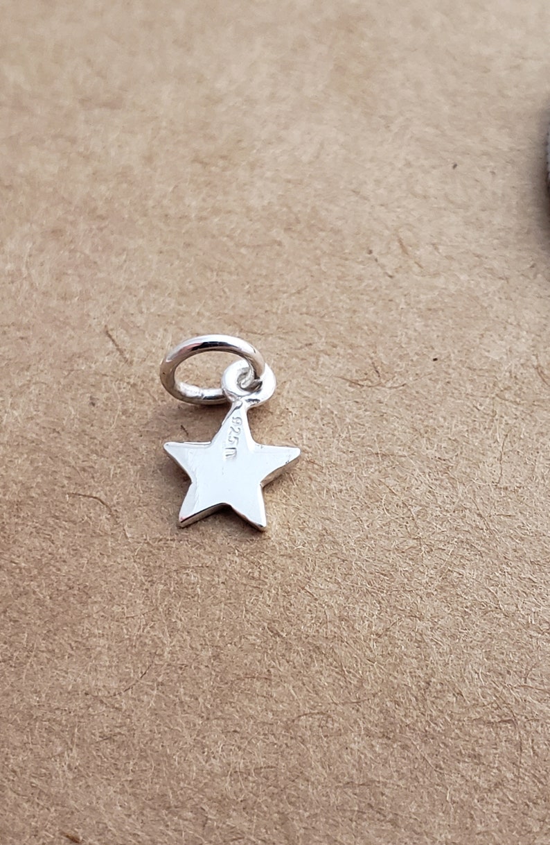 May include: A silver star charm with a jump ring. The back of the charm has the inscription "925".