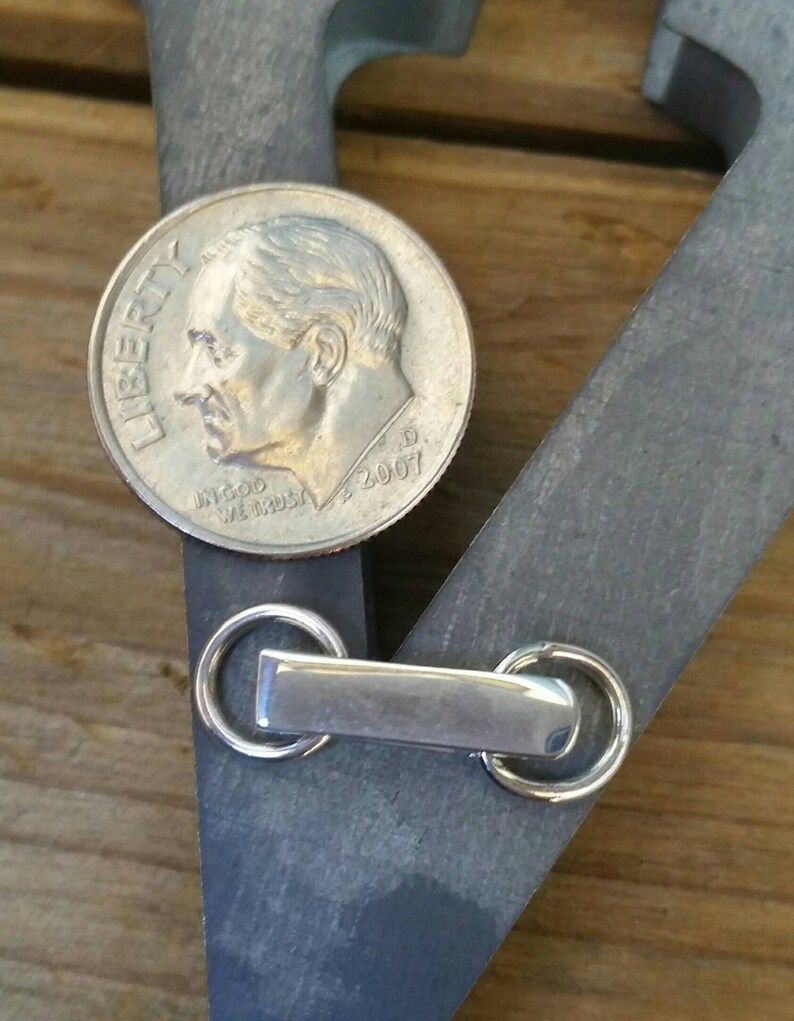 Peut inclure: Une pi&egrave;ce de monnaie argent&eacute;e de 2007 est pos&eacute;e sur un objet en m&eacute;tal gris fonc&eacute; avec une barre rectangulaire et deux anneaux circulaires. La pi&egrave;ce est &agrave; c&ocirc;t&eacute; de l'objet m&eacute;tallique, sur une surface en bois.