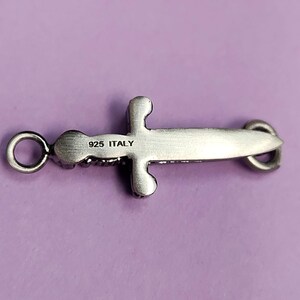 May include: Silver sword pendant charm with a detailed design and a loop for attaching to a chain or bracelet. The back of the charm is engraved with "925 ITALY".