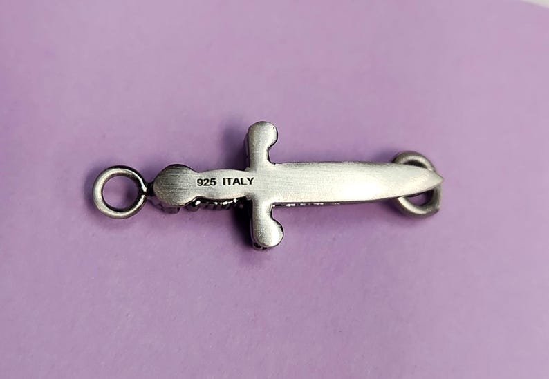 May include: Silver sword pendant charm with a detailed design and a loop for attaching to a chain or bracelet. The back of the charm is engraved with "925 ITALY".