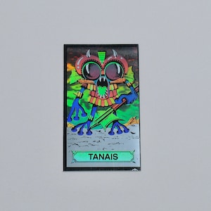 Puede incluir: Una carta de intercambio holográfica con un monstruo verde, azul y rojo con ojos grandes y una espada. La carta tiene la palabra "TANAIS" impresa en ella.