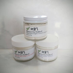 May include: Three glass jars of aluminum-free deodorant with white lids. Each jar has a label with the text "DEB'S" and product information. The top jar reads "Natural Scent of Organic Coconut Oil." The other jars are scented with sweet orange & lemon and lavender essential oil.