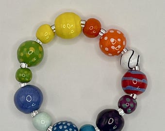 May include: A circular bracelet composed of multicolored beads in various sizes and patterns, including solid yellow, green, blue, and purple, alongside orange with white dots, red with blue stripes, and blue with white dots, separated by small silver spacers.