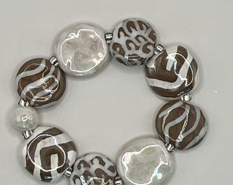 May include: A stretch bracelet composed of round, irregular ceramic beads. The beads feature a mix of glossy white, brown and white striped, and brown and white leopard print patterns, separated by small silver-toned metallic spacer beads.