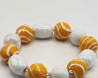 May include: A stretch bracelet featuring alternating round beads in bright orange with white swirl patterns and smooth, iridescent white oval beads. The beads are strung together on a flexible cord, creating a circular shape with a glossy finish.