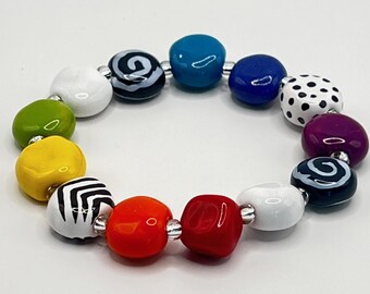 May include: A stretch bracelet composed of multi-colored, irregular, rounded beads. The beads feature solid colors including red, orange, yellow, lime green, white, turquoise, and purple, alongside patterned beads with black and white stripes, swirls, and dots.