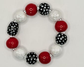 May include: A circular bracelet composed of alternating spherical beads. The beads feature a repeating pattern of solid red, solid white with a pearlescent finish, and black with white polka dots, all separated by small silver-toned spacer beads.