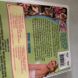 May include: DVD cover for the movie "A Cinderella Story" featuring Hilary Duff. The cover is green with a pink and white Cinderella-themed design. The text "Hilary Duff sparkles in the must-see toon movie of the year!" is printed on the cover.