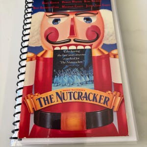 May include: A spiral-bound notebook featuring a cover illustration of a red nutcracker soldier. The text reads Family Entertainment, The Nutcracker, and lists names including Darci Kistler and Macaulay Culkin, with a quote from Newsweek.