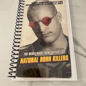 May include: A vintage movie poster for the film "Natural Born Killers" featuring Woody Harrelson and Juliette Lewis. The poster has a yellow and black title with the text "The media made them superstars."