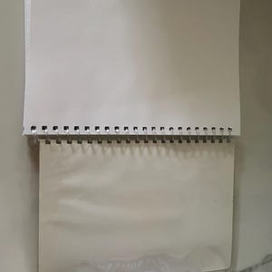 May include: A white spiral bound notebook with a clear plastic cover. The notebook is blank and ready to be used for writing, drawing, or sketching.
