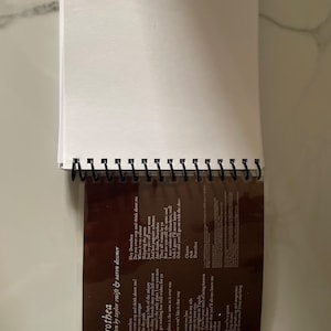 May include: A close-up of a brown notebook with a plastic sleeve covering the lyrics to the song "Dorothea" by Taylor Swift. The lyrics are printed in white text and include the lines "Hey Dorothea, Do you ever stop and think about me?" and "This place is the same as it ever was."
