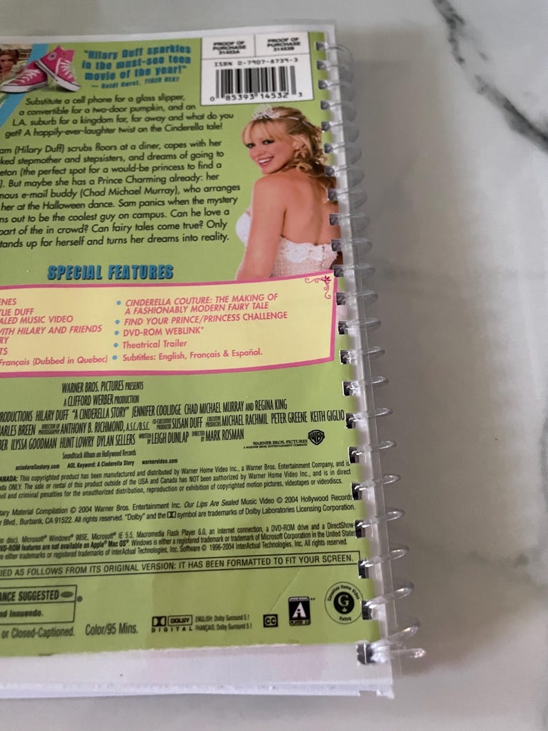 May include: DVD cover for the movie "A Cinderella Story" featuring Hilary Duff, Chad Michael Murray, and Jennifer Coolidge. The cover is pink and green with a white border. The title of the movie is in large, white letters. The cover also includes a barcode and a list of special features.