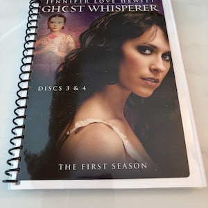 May include: A spiral-bound media case featuring the television series Ghost Whisperer, The First Season, Discs 3 & 4. The cover displays a portrait of Jennifer Love Hewitt and a smaller figure of a child holding a flower against a dark background.