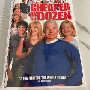 May include: A spiral-bound notebook featuring the movie poster for "Cheaper by the Dozen." The poster shows a group of people, including Steve Martin, with the movie title in large red letters. The notebook has the text "A FUN FILM FOR THE WHOLE FAMILY!"