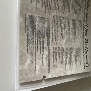 May include: A close-up of a book with a white background and a torn page. The text on the page is a song lyric from the song "Coney Island" by Taylor Swift featuring The National. The lyrics are: "Lost again with no surprises, Disappointments, close your eyes and it gets colder and colder, When the sun goes down."