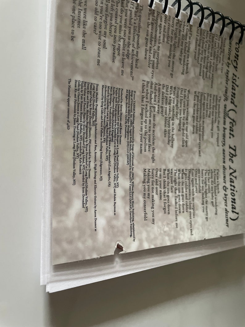 May include: A close-up of a book with a white background and a torn page. The text on the page is a song lyric from the song "Coney Island" by Taylor Swift featuring The National. The lyrics are: "Lost again with no surprises, Disappointments, close your eyes and it gets colder and colder, When the sun goes down."