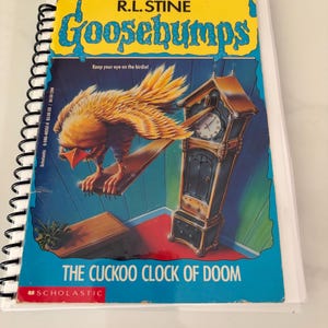 May include: A spiral-bound book titled Goosebumps: The Cuckoo Clock of Doom by R.L. Stine. The cover features a yellow bird with an orange beak perched on a wooden plank next to a tall, dark brown grandfather clock against a blue wall.