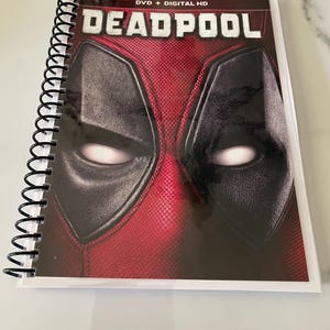 May include: A spiral bound notebook with a Deadpool movie cover. The cover features a close-up of Deadpool's face with the text "DVD + DIGITAL HD DEADPOOL" at the top.