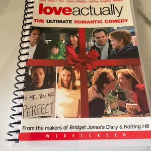 May include: A spiral-bound DVD of the romantic comedy "Love Actually." The cover features a collage of actors and the text "THE ULTIMATE ROMANTIC COMEDY." Below, a sign reads "TO ME, YOU ARE PERFECT." The DVD is from the makers of "Bridget Jones's Diary & Notting Hill."