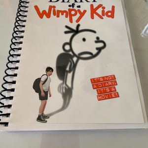 May include: A spiral-bound book with the title "DIARY of a Wimpy Kid" in orange letters. The cover features a cartoon drawing of a boy and the text "IT'S NOT A DIARY, IT'S A MOVIE!"