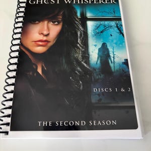 May include: A spiral-bound media case featuring the Ghost Whisperer television series, second season, discs 1 and 2. The cover displays a portrait of Jennifer Love Hewitt alongside a dark, atmospheric scene of a silhouette standing near trees.