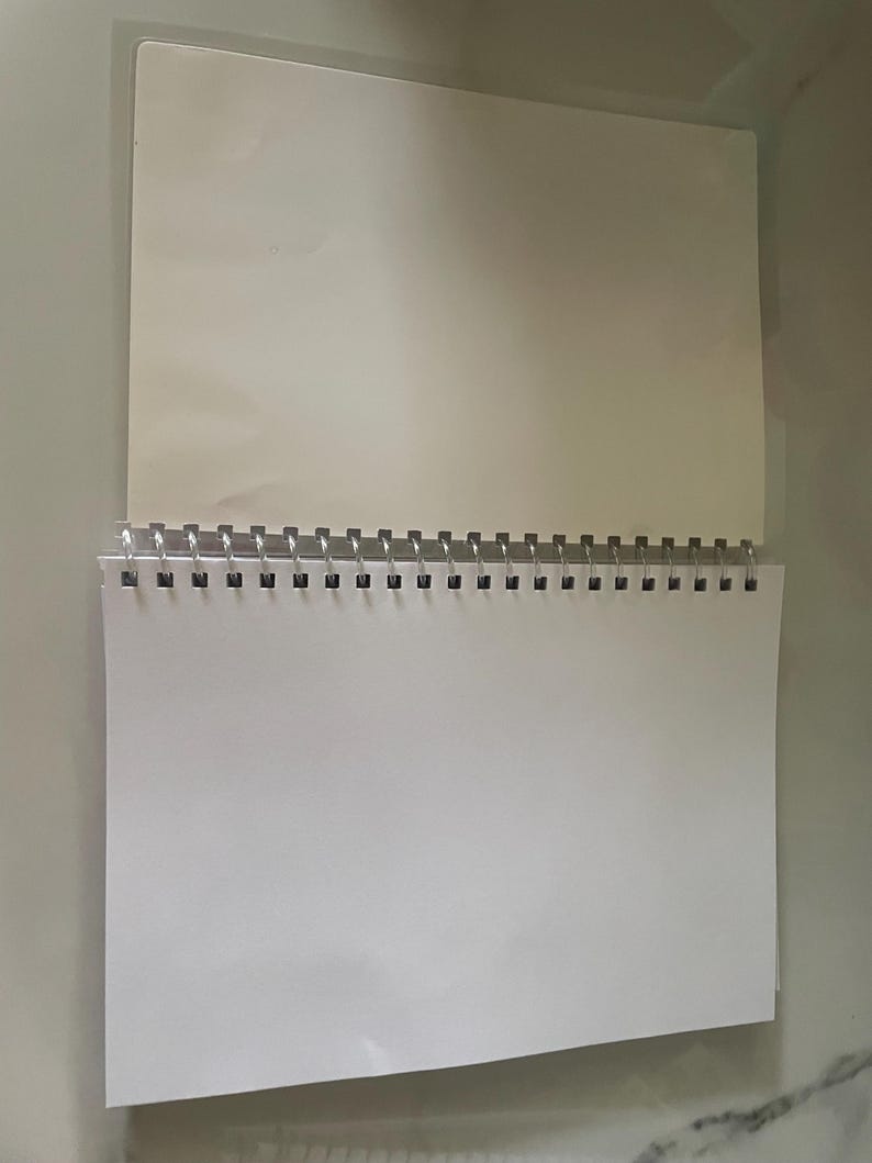 May include: A white spiral bound notebook with a clear plastic cover.