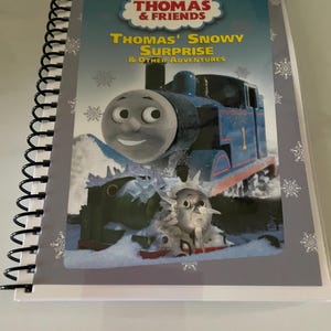 May include: A blue and gray spiral bound book with a cover featuring Thomas the Tank Engine. The title of the book is "Thomas' Snowy Surprise & Other Adventures".