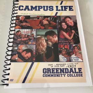 May include: A spiral-bound notebook with a cover featuring the text "CAMPUS LIFE" in blue and yellow. The cover includes images of people and the text "GREENDALE COMMUNITY COLLEGE". The notebook is on a white surface.