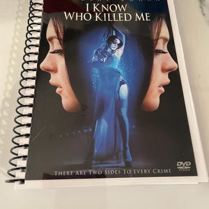 May include: A spiral-bound DVD case for the movie "I Know Who Killed Me" starring Lindsay Lohan. The cover features a central image of a woman in a blue dress, flanked by two profile portraits of a woman. The text "THERE ARE TWO SIDES TO EVERY CRIME" is also visible.