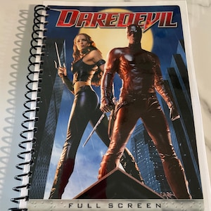 May include: A spiral bound notebook with a Daredevil movie poster cover featuring a red and black superhero character and a woman in black clothing. The poster has the text "Daredevil" and "Full Screen".