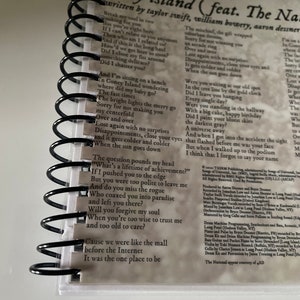 May include: A close-up of a spiral bound notebook with lyrics from the song "Coney Island" by Taylor Swift featuring The National. The lyrics are written in black ink on a white background. The lyrics include the lines "Break my soul in two" and "The question pounds my head, "What's a lifetime of achievement?"