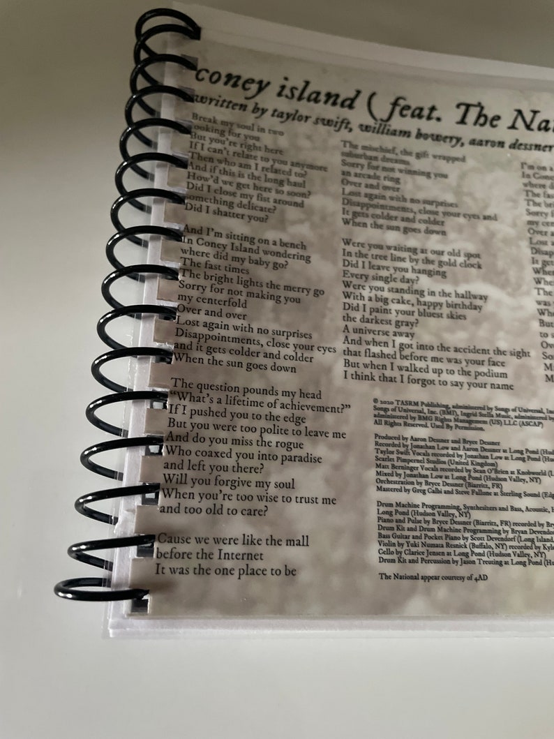 May include: A close-up of a spiral bound notebook with lyrics from the song "Coney Island" by Taylor Swift featuring The National. The lyrics are written in black ink on a white background. The lyrics include the lines "Break my soul in two" and "The question pounds my head, "What's a lifetime of achievement?"