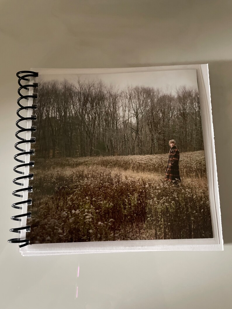 May include: A person wearing a plaid coat walks through a field of tall grass and trees in the background. The photo is taken on a cloudy day.
